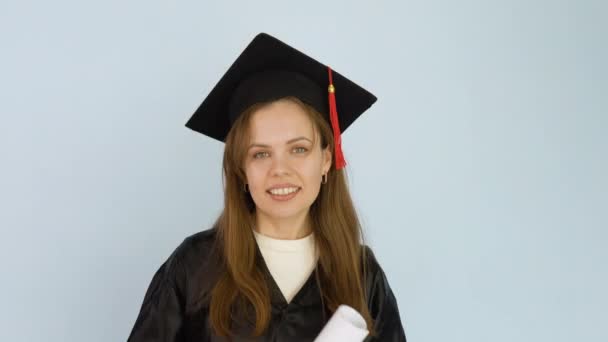 Νεαρή φοιτήτρια με μαύρη ρόμπα και καπέλο μάστερ με δίπλωμα τριτοβάθμιας εκπαίδευσης. Ένας απόφοιτος πανεπιστημίου χορεύει με ένα δίπλωμα στα χέρια της και το πετάει και το πιάνει. Λευκό φόντο — Αρχείο Βίντεο
