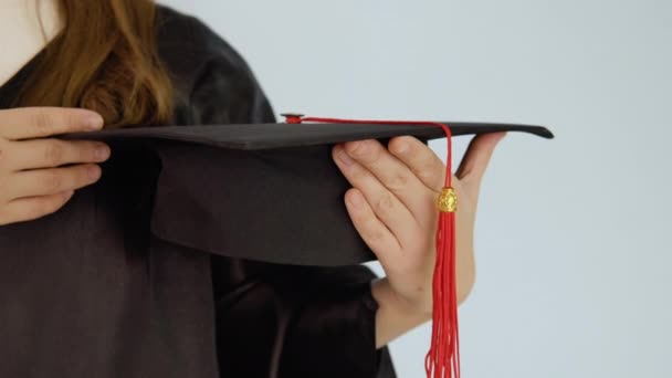 Un sombrero negro cuadrado con un cepillo rojo en las manos de un graduado caucásico con uñas naturales pulcras. Primer plano de disparo de un sombrero y las manos. Fondo blanco — Vídeos de Stock