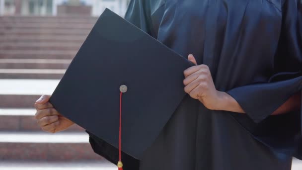 正方形的主礼帽垂直地放在一位非洲裔美国女大学毕业生的手里，背景在楼梯的外面. — 图库视频影像