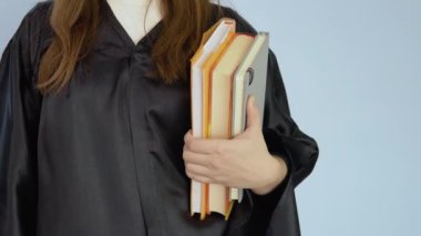 Siyah cüppeli bir kız öğrencinin elinde birkaç ders kitabı dikey pozisyonda duruyor. Beyaz arkaplanda kitapların ve ellerin görüntüsü.