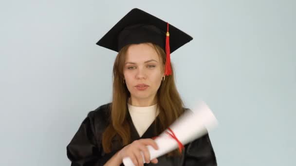 Μια απόφοιτος πανεπιστημίου χορεύει με ένα δίπλωμα στα χέρια της. Νεαρή φοιτήτρια με μαύρη ρόμπα και καπέλο μάστερ κατέχει σε όρθια θέση δίπλωμα τριτοβάθμιας εκπαίδευσης. Λευκό φόντο — Αρχείο Βίντεο