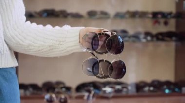 Rafın arka planında gözlüklü bir kadın elinde üç çift gözlük.