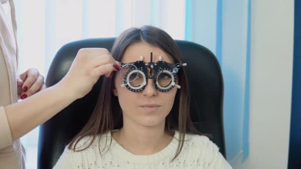 Lékař instaluje sklo do skiascope pro mladou bělošku v útulném bílém svetru na oční klinice — Stock video