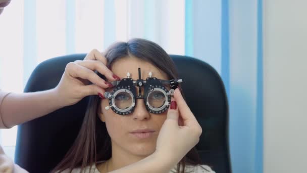 De dokter zet een skiascoop op voor een jonge vrouw in een knusse witte trui in een optische kliniek — Stockvideo