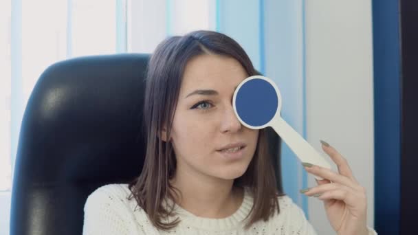 Mladá běloška v útulném bílém svetru v kanceláři oftalmologů na oční klinice odpovídá na otázky lékařů během vyšetření zraku. — Stock video