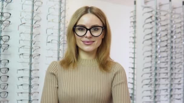 Attraktive junge blonde Frau mit transparenter Brille und schwarzem Rahmen für die Sehkorrektur vor einem Spiegel in einem Brillengeschäft und Blick auf das KameraVision-Korrekturkonzept — Stockvideo