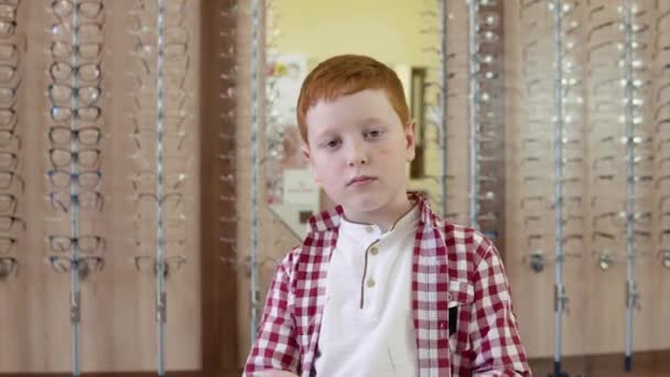 Red-haired boy in a plaid red and white shirt wears sunglasses with octagonal lenses looking straight into the camera and imagining himself a cool guy — Stock Video