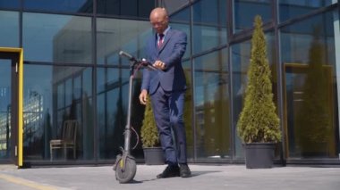 Klasik mavi takım elbiseli Afro-Amerikalı bir adam elektrikli scooter 'a biner ve modern ayna binasının yakınındaki bir caddede gezer. Alt görünüm tam uzunlukta