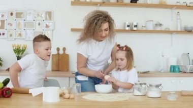 Kız ve anne bir kasede yumurta kırıyorlar. Yaratıcılık ve çocuklar için yemek pişirme. Annelik. Beyaz tişörtlü ve kot pantolonlu sarışınların ailesi