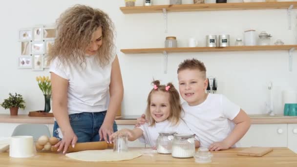 子供と家族のレジャー。子供のための創造性と料理。母親。白いTシャツのブロンドの家族が白いキッチンで生地からクッキーを切り取りました — ストック動画