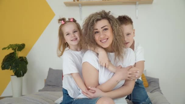 Mamma con figlia e figlio si abbracciano seduti in una stanza accogliente. Bellissimo ritratto di famiglia. Colori bianco e giallo. Minimalismo — Video Stock