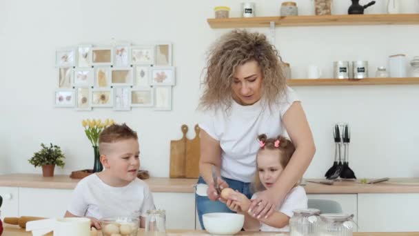 Kinder mit Mutti in der Küche im skandinavischen Design backen. Familie in weißen T-Shirts und Jeans — Stockvideo