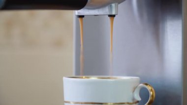 Kahve makinesinden küçük beyaz bir porselen fincana altın kaplama kahve dökme işlemi.