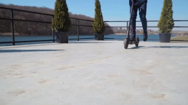 Ein Mann im klassischen Businessanzug und blauen Schuhen fährt mit einem Elektroroller am Fluss entlang. Ansicht von unten in voller Länge — Stockvideo