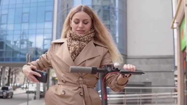 Una mujer joven alquila scooter eléctrico utilizando la aplicación de teléfono móvil. Aplicación de teléfono turístico. Aparatos modernos para jóvenes y empresarios — Vídeos de Stock