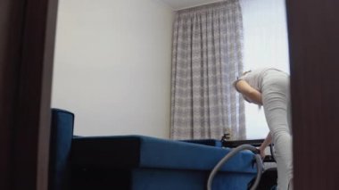 Temizliği kolaylaştıran teknolojiler. Modern ev aletleri. Kadın ev hanımı döşeme mobilyalarının temizlenmesi için özel bir hortumla kanepeyi süpürüyor.