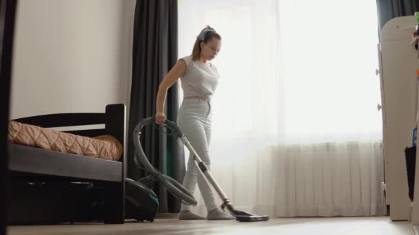 Vacuuming lantai oak cahaya dengan air. Teknologi yang memfasilitasi pembersihan basah. Wanita muda ibu rumah tangga dengan pakaian retro biru muda dengan gaya pin-up menggunakan vacuum cleaner modern — Stok Video