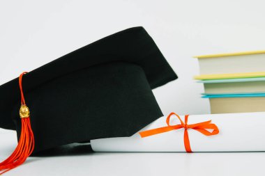 Kırmızı püsküllü siyah kare mezuniyet şapkası bir diploma ve bir yığın kitabın üzerinde yatıyor. Eğitim kavramı