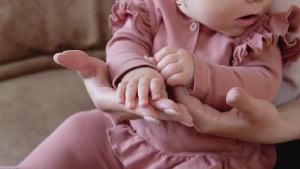 Bebeğin elleri annenin ellerinde. Ellerin yakın görüntüsü. Mavi gözlü, pembe takım elbiseli küçük kız annesinin kucağında oturuyor. — Stok video
