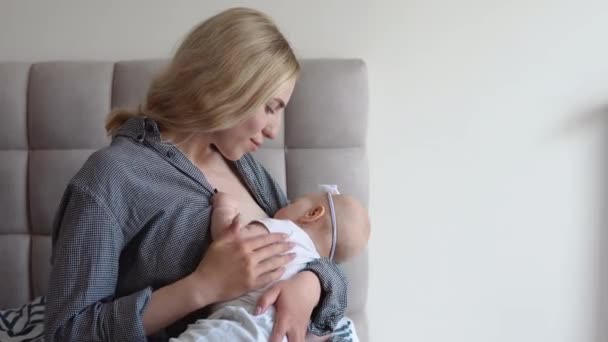 Mutter stillt ihre kleine Tochter, während sie auf dem Bett sitzt. Seitenansicht. Babypflege — Stockvideo