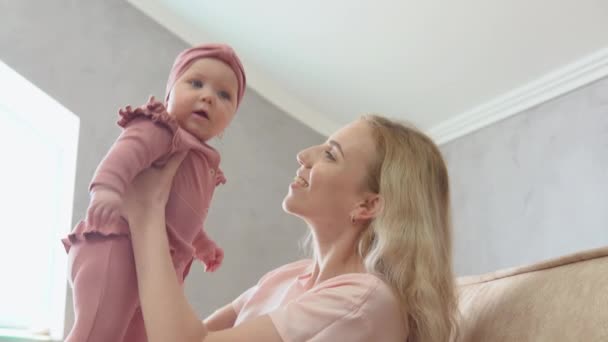 De moeder houdt de babydochter vast en kust haar vrolijk op de wang. — Stockvideo