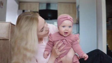 Anne ve bebek kız mavi gözlü ve sarı saçlı kameranın önünde oturuyorlar.