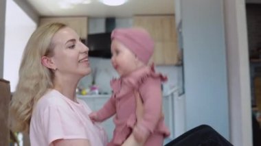 Sarı saçlı, mavi gözlü, pembe elbiseli anne ve bebek modern mutfak setinin arka planında iyi eğlenceler.
