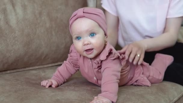 Egy szőke hajú, kék szemű, rózsaszín ruhás kislány fekszik a hasán, és különböző irányokba hintázik. Gyermekfejlődés az élet első évében — Stock videók