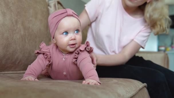 A mãe acaricia os bebés. Desenvolvimento infantil no primeiro ano de vida. Uma menina com cabelo loiro e olhos azuis em roupas cor-de-rosa está em sua barriga e balança em direções diferentes — Vídeo de Stock