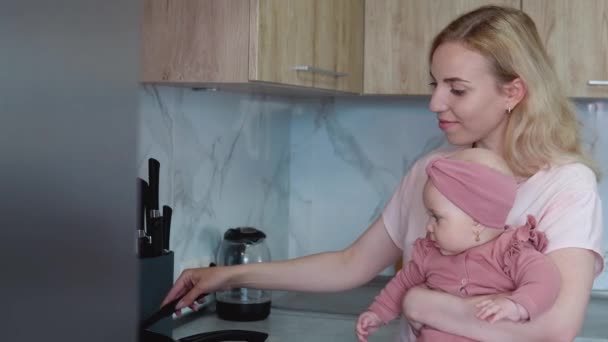 Moeder bereidt voedsel met baby in haar armen. Dagelijkse moeders. Moeders huiswerk — Stockvideo