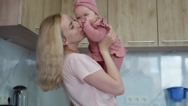 Mutter spielt mit Baby, das sie in der Küche im Arm hält. Alltagsmütter. Hausaufgaben für Mütter — Stockvideo