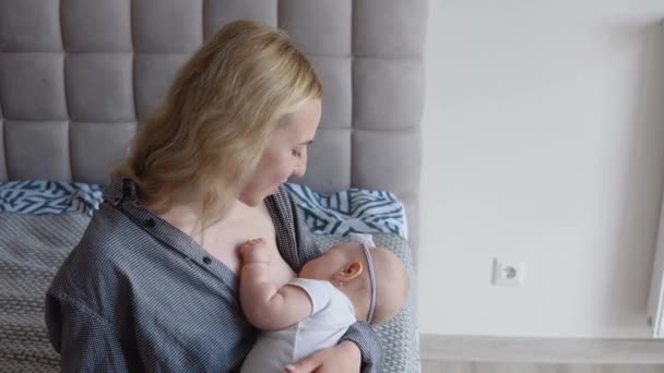 Mother breastfeeds her baby daughter while sitting on the bed. Side view. Baby care — Stock Video
