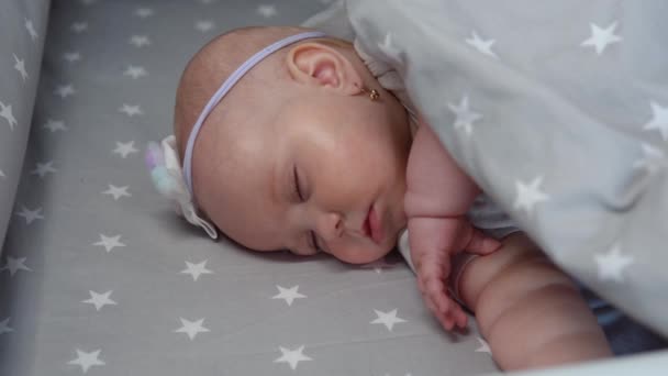 Děvčátko spí v kolébce s šedým povlečením a ústy dělá sající pohyb. Dítě sní o kojení — Stock video