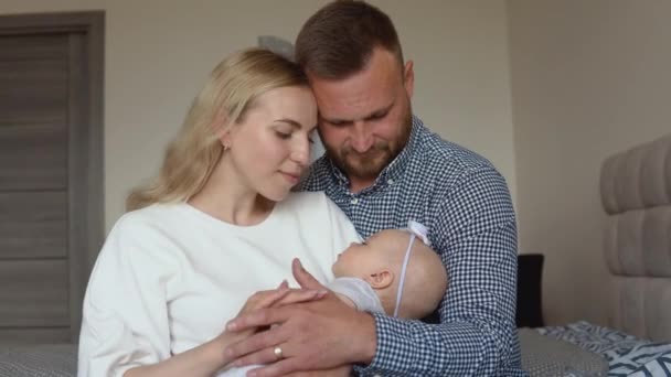 Mor och far kramar och beundrar sitt barn medan barnet sover i armarna på modern. Faderskap och moderskap. Traditionell familj — Stockvideo