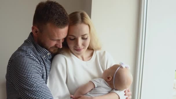 Madre e padre abbracciano e ammirano il loro bambino mentre dorme tra le braccia della madre. Paternità e maternità. Famiglia tradizionale — Video Stock