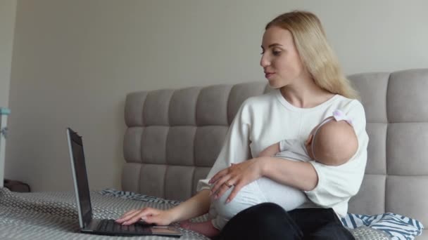 Egy kislány az anyja karjaiban alszik, míg az anyja otthon dolgozik egy laptopon. A szülési szabadsággal kapcsolatos távmunka — Stock videók