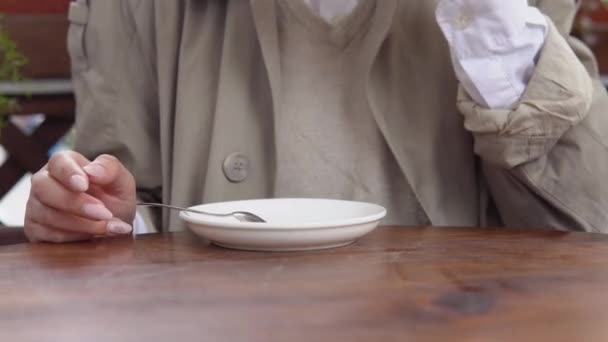 Mladá žena s úhlednou manikúrou v béžových a bílých neformálních šatech zvedne bílý porcelánový šálek kávy a položí ho zpátky na talíř. Detailní pohled na ruce a poháry — Stock video