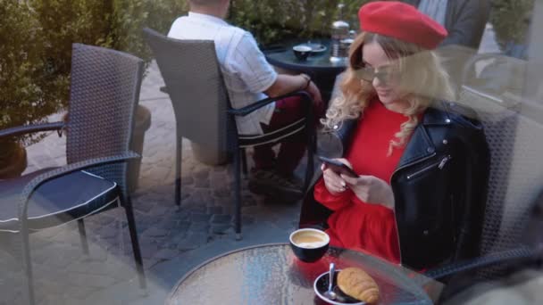 Pausa para café com croissant. Jovem urbana moderna trabalhando on-line no telefone celular no terraço restaurante acolhedor — Vídeo de Stock