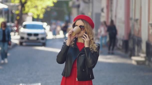 Молодая женщина посреди улицы разговаривает по мобильному телефону и пьет кофе на вынос во время работы в течение дня. — стоковое видео