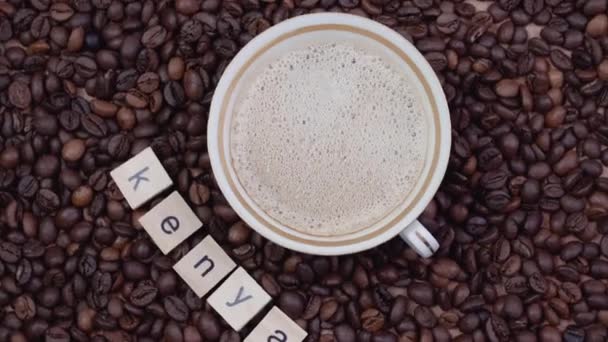 Cup of coffee on a background of coffee beans with the word Kenya outlined. Production, export and import of coffee. Top view — Stock Video