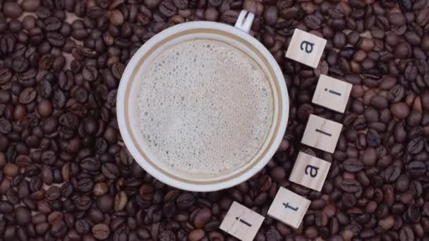 Tazza di caffè su sfondo di chicchi di caffè con la parola Italia delineata. Vista dall'alto. Video verticale — Video Stock