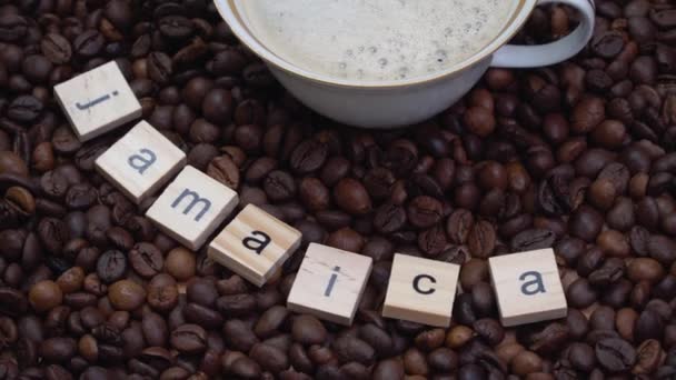 Κόκκοι καφέ με την επιγραφή Τζαμάικα και ένα φλιτζάνι πορσελάνη με καφέ πάνω τους. Χώρα παραγωγής καφέ — Αρχείο Βίντεο