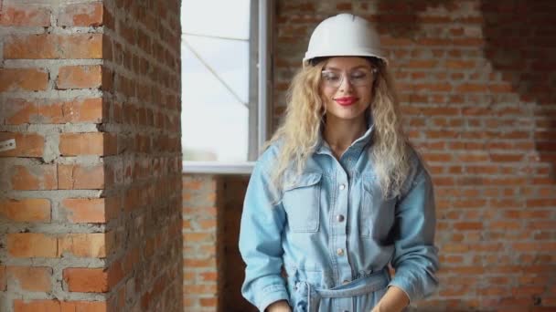 Процесс строительства дома мечты. Жилье для молодых семей. Молодая женщина в рабочем шлеме и джинсовой одежде и очках стоит на стройке. — стоковое видео