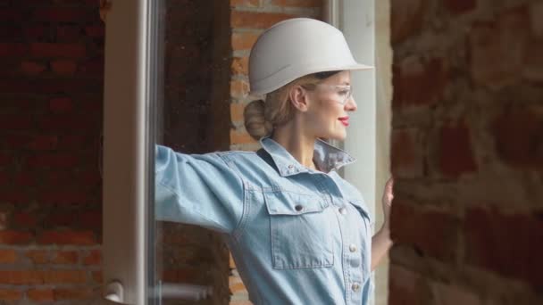 Vrouwelijke architect kijkt uit het raam op een bouwplaats. Het proces van woningbouw voor het gezin — Stockvideo
