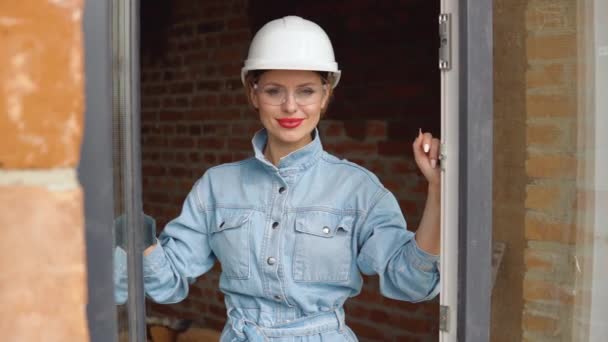 Una arquitecta o albañil se encuentra en una ventana abierta en una obra de construcción. El proceso de construcción de viviendas para la familia — Vídeos de Stock