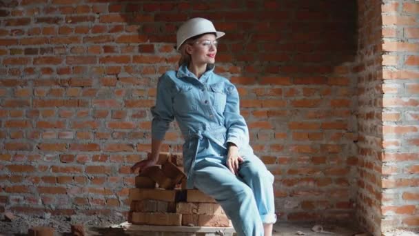 Kvinnlig arkitekt eller murare som sitter på en hög med tegelstenar på en byggarbetsplats. Processen att bygga bostäder för familjen. Byggnadsmaterial — Stockvideo