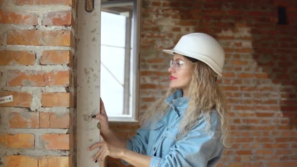 Ženský architekt nebo zedník stojí v nově postaveném domě s neošetřenými zdmi a kontroluje stěny speciálním zařízením.