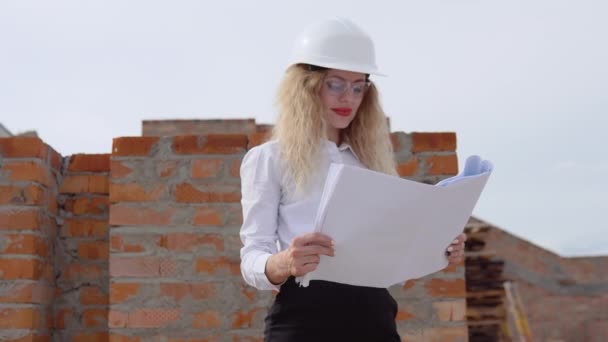 Female architect in business attire standing outdoors at construction site. The architect reads the architectural plan — Stock Video