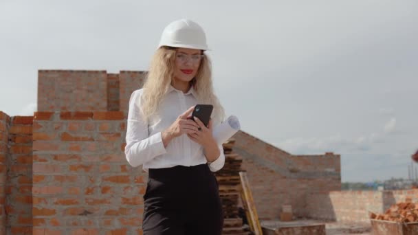 Kvinnlig arkitekt i affärskläder står i ett nybyggt hus och pratar i telefon. Modern teknik inom de äldsta yrkena — Stockvideo