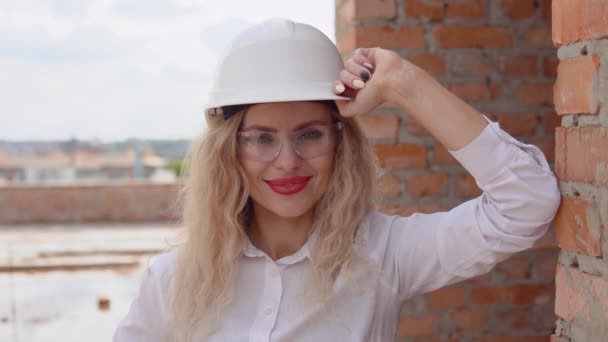 Vrouwelijke architect in bedrijfskleding en een witte helm staat op de bouwplaats — Stockvideo